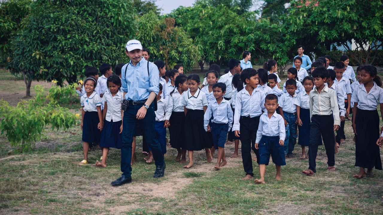 Group of elementary school students walking outdoors with a teacher in uniform